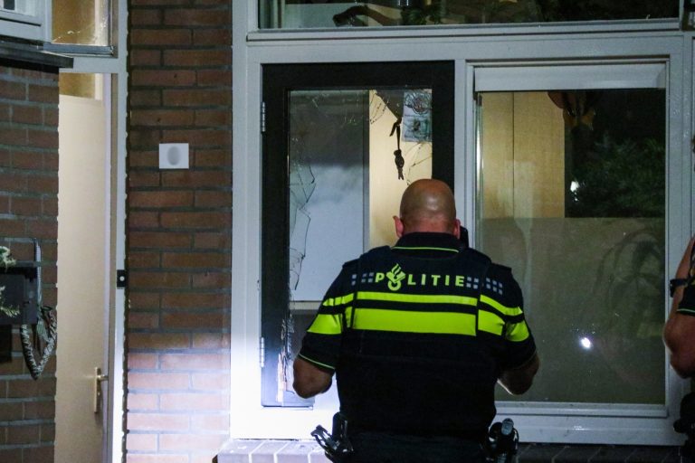 Politieagent staat voor een raam dat kapot is na een explosie op de Rabarberdreef